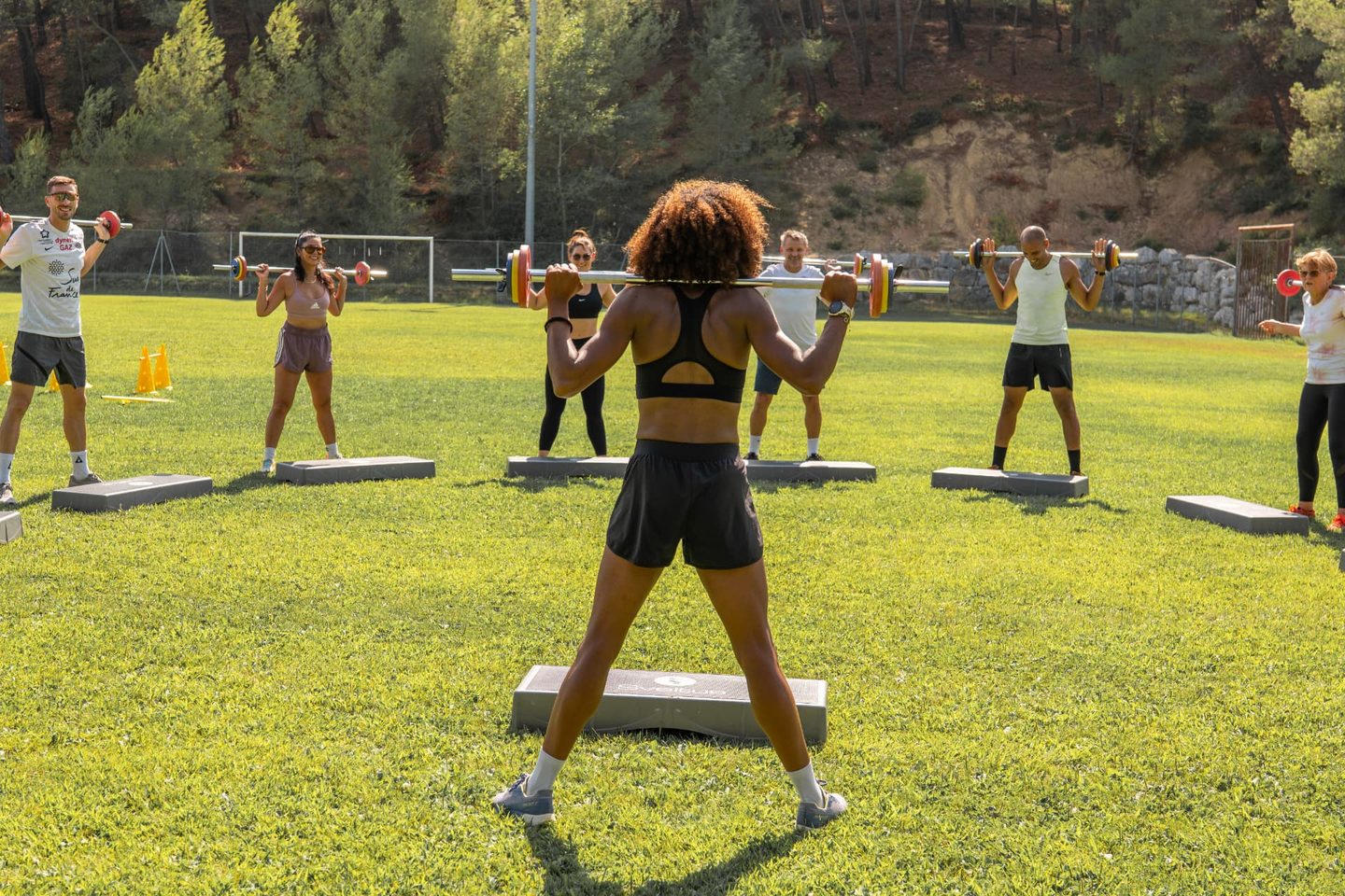 Séance de renforcement musculaire en plein air : Aurélie Kamga, coach sportive, guide un groupe adulte en squat avec barre sur le stade Christian Bougette à Montferrier-sur-Lez.