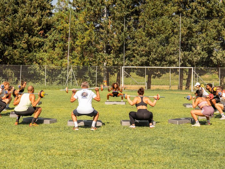 Groupe d'adhérents de l'association La Meute de Montferrier en position de squat avec barre, sur steps, pendant un circuit de renforcement musculaire en extérieur